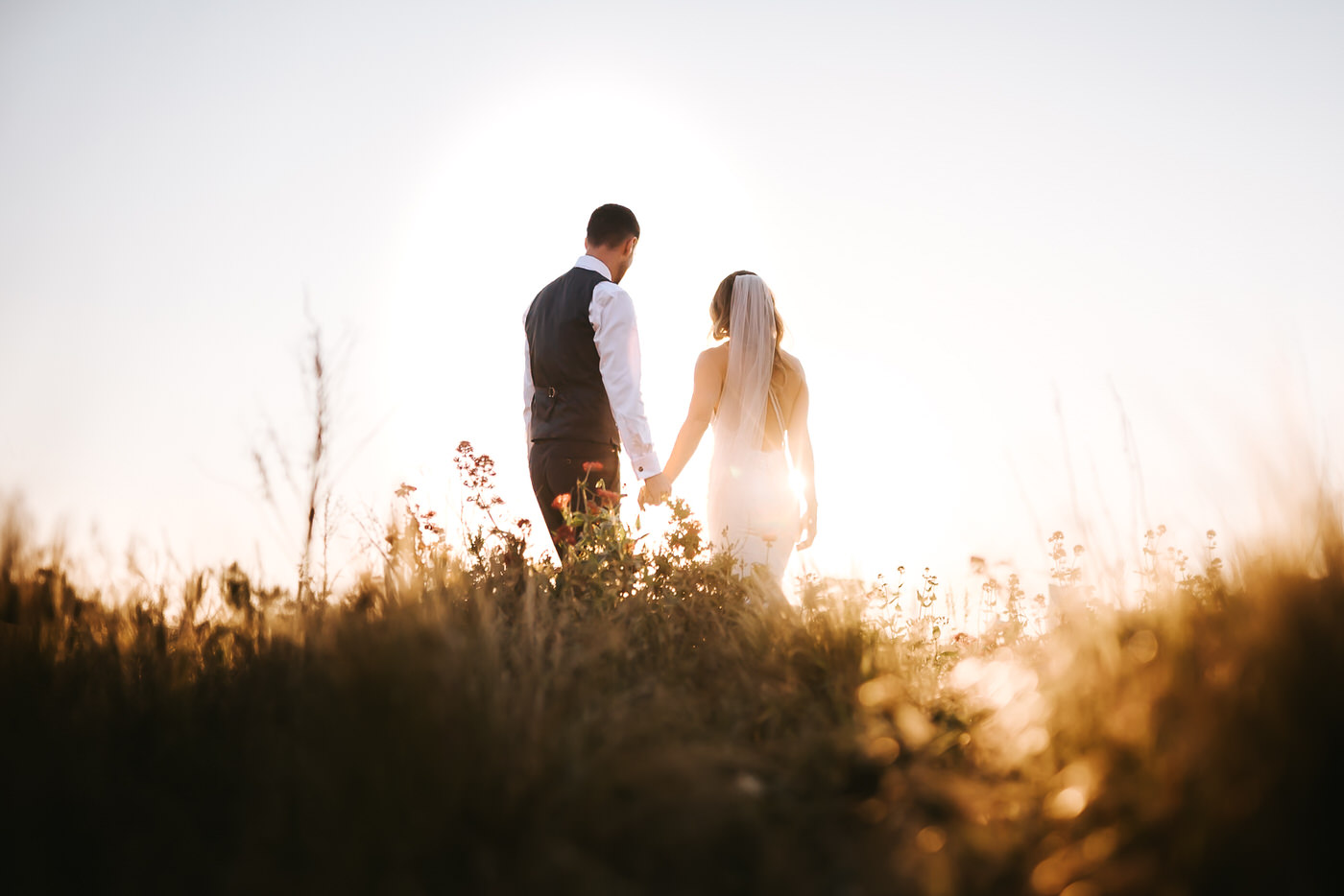 asylum chapel wedding bride andgroom walkinf away from the camera holding hands backlit by the setting sun