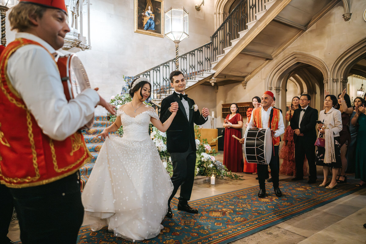 ashridge house wedding couple going down the grand staircase with drummers drumming and guests cheering around them