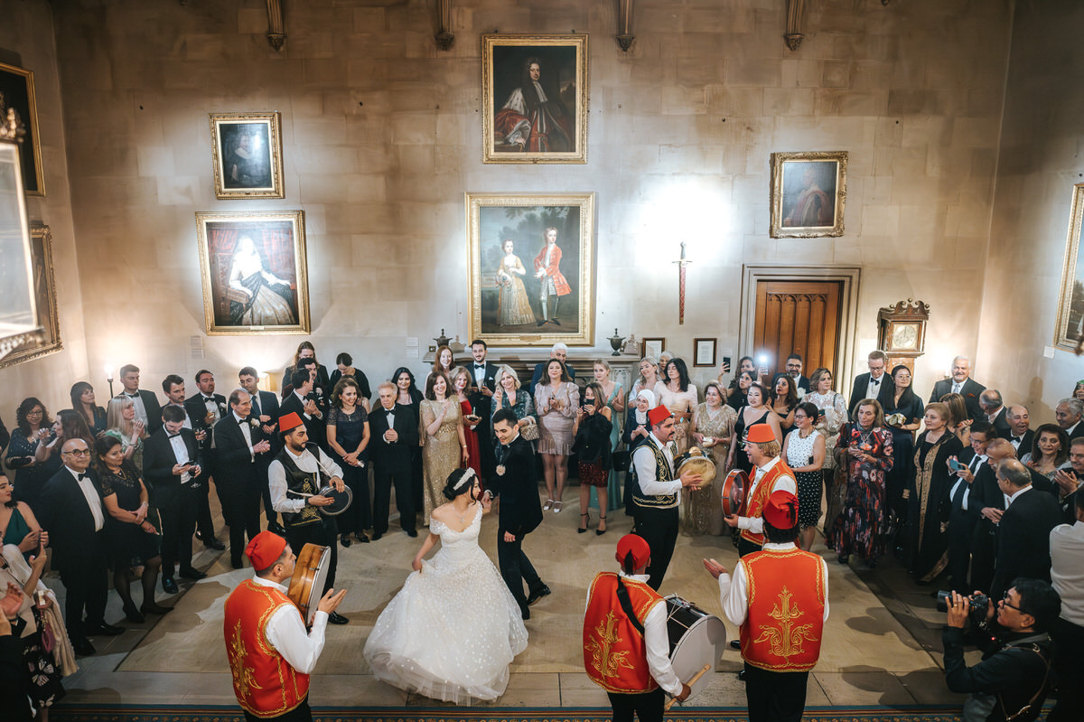 ashridge house wedding wide shot of newlyweds dancing in the great hall surrounded by cheering guests