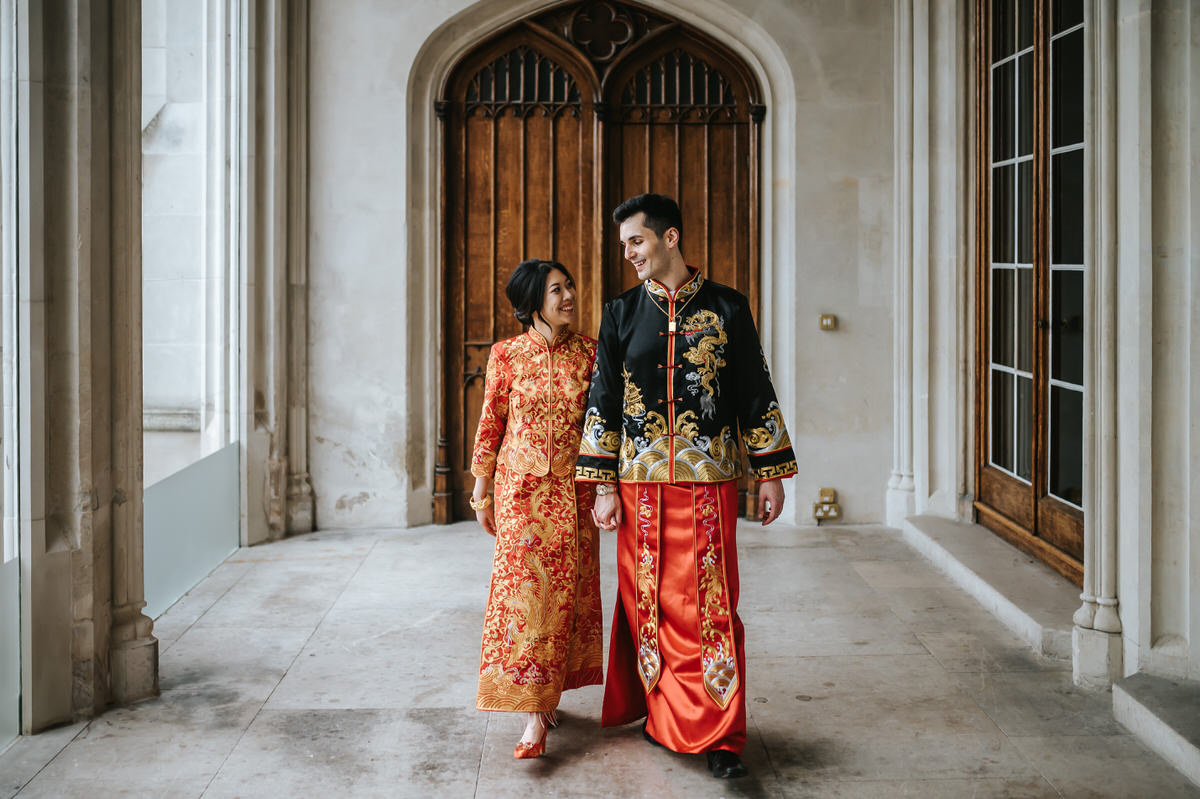 ashridge house wedding couple walking on the terrace looking at each other and smiling wearing traditional chinese red wedding outfits
