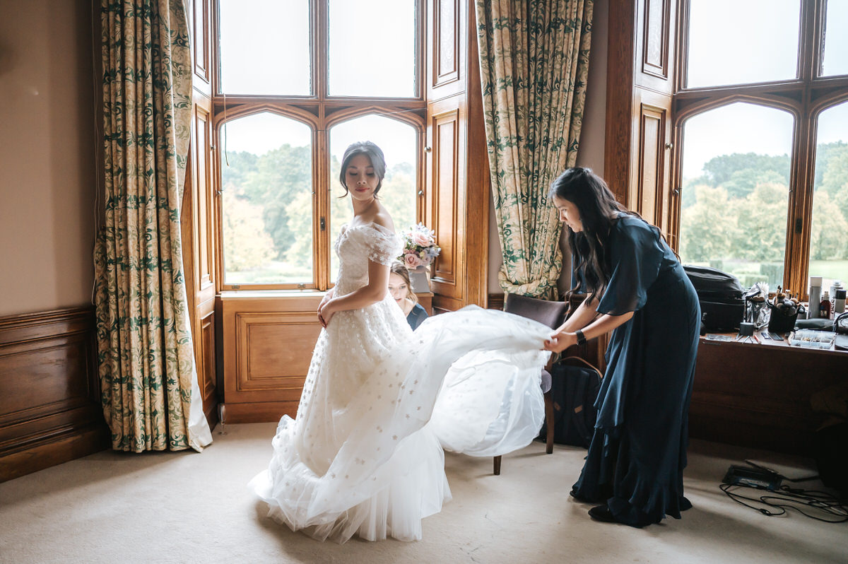 ashridge house wedding getting ready bridesmaid fluffing the wedding dress