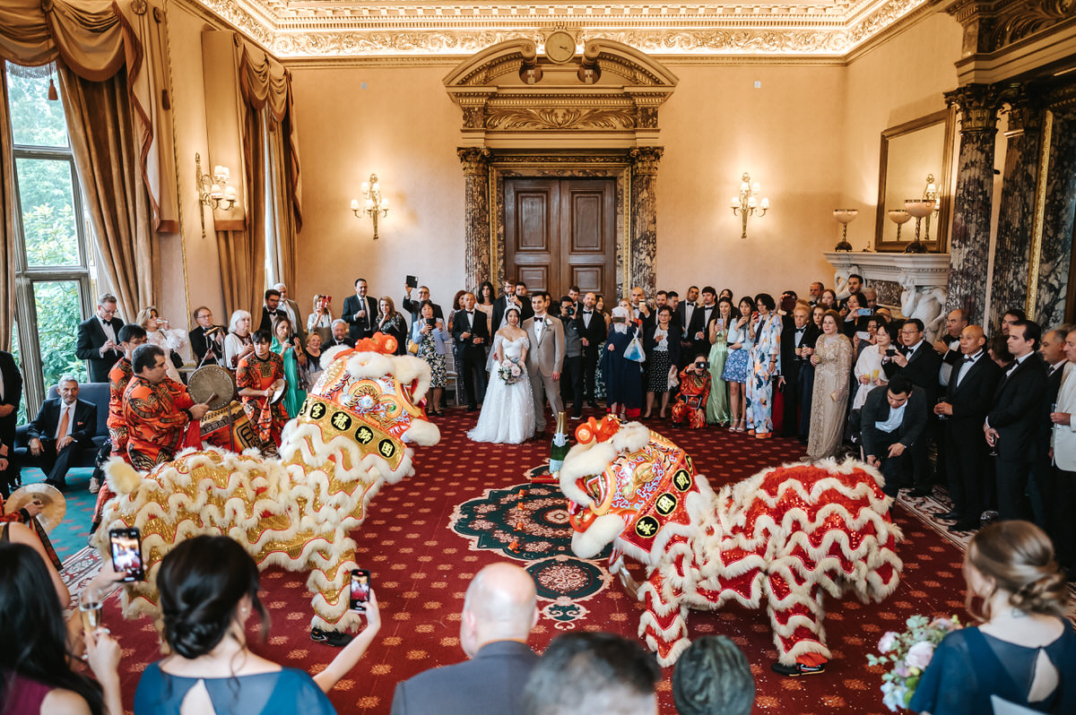 ashridge house wedding chinese dragon dance with bride and groom in the centre surrounded by guests and two giant dragons