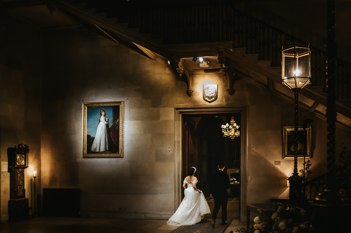 ashridge house wedding bride and groom walking through grand hall with their backs to the camera