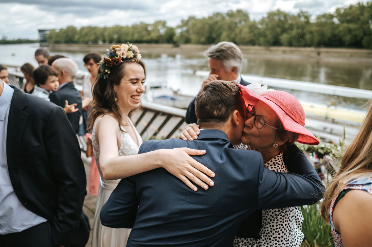 london rowing club wedding groom kissing his mum on the balcony with the river in the background