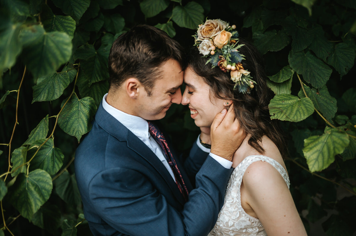 london rowing club wedding bride and groom smiling at eachother surrounded by green leaves