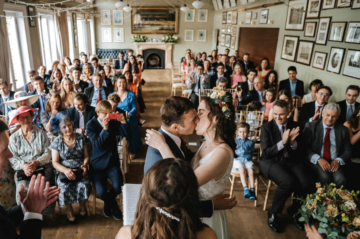 london rowing club wedding wide shot of the first kiss with guestd cheering in the background